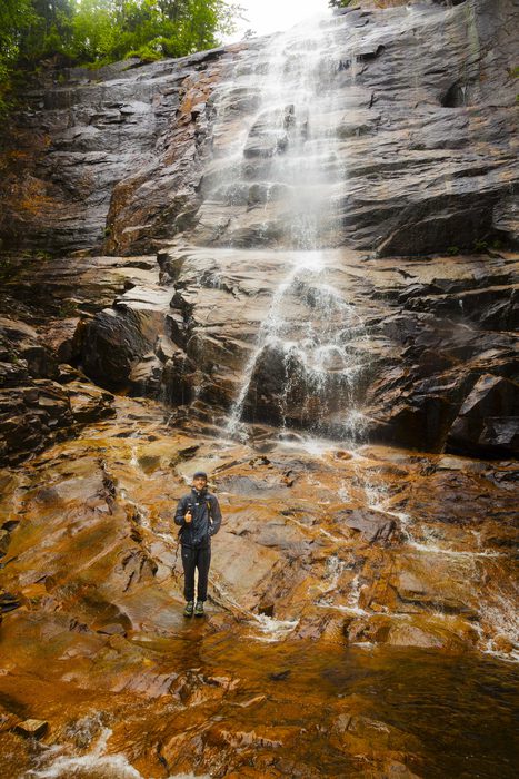 A tiny figure giving a thumbs up dwarfed by a massive waterfall in Crawford Notch